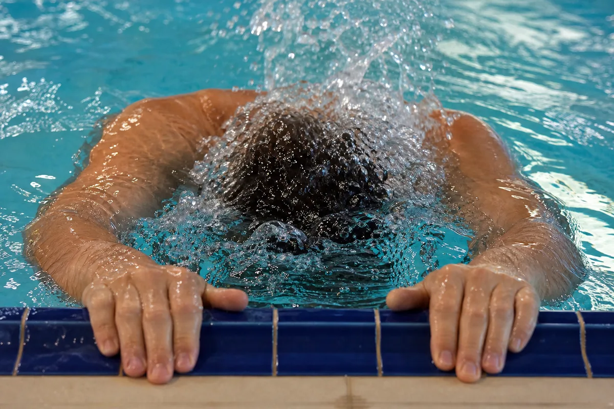 Nageur accroché au bord du bassin, visage immergé, soufflant un chapelet de bulles lors d&rsquo;un exercice de respiration