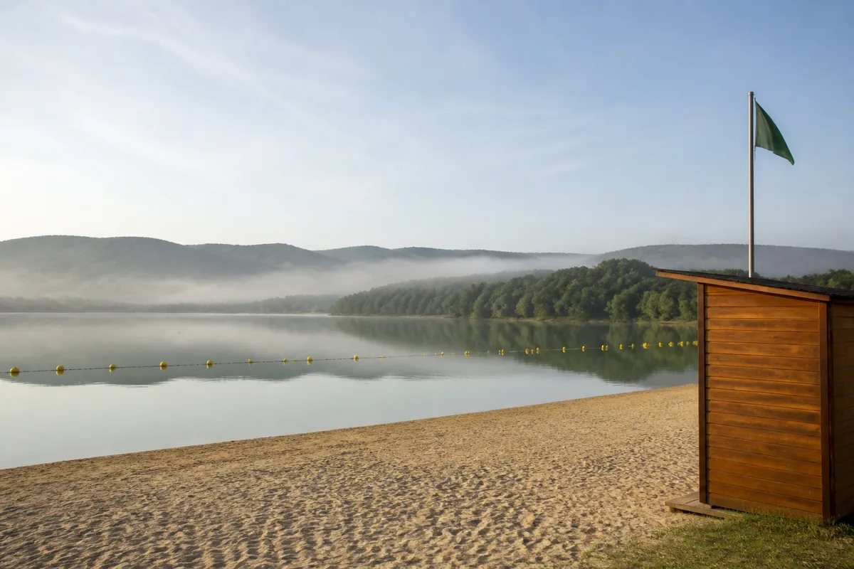 Lac calme au petit matin avec un poste de secours et une zone de baignade balisée par des bouées jaunes