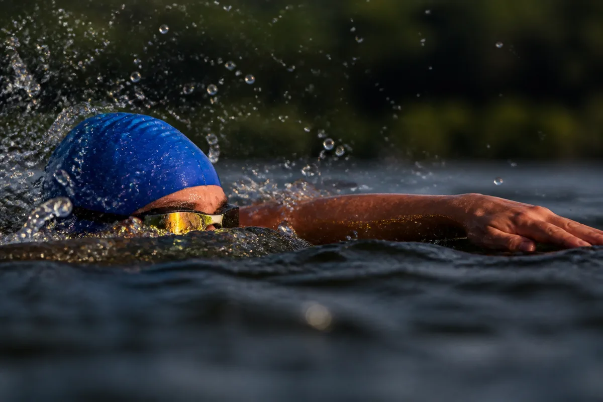 Nageur en combinaison relevant les yeux hors de l&rsquo;eau pour se repérer, gouttes en suspension, lumière rasante du matin
