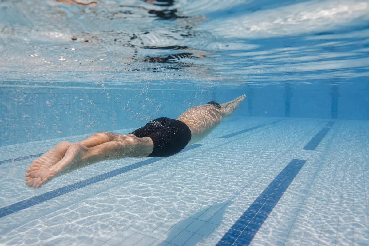 Nageur en ondulation sous la surface d’un bassin, vu de dos, jambes jointes